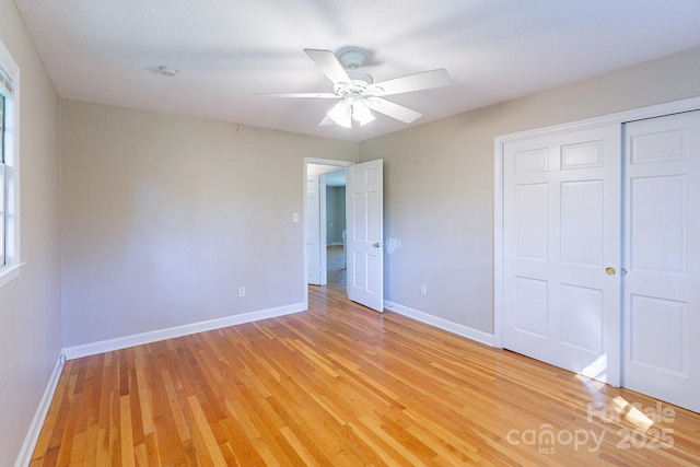 unfurnished bedroom featuring baseboards, ceiling fan, a closet, and light wood-style floors