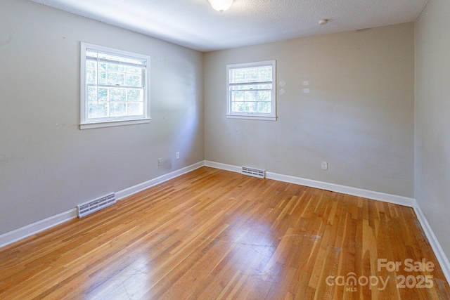 empty room featuring light wood finished floors, baseboards, visible vents, and a textured ceiling