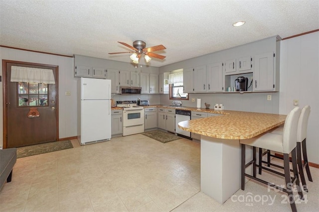 kitchen with white appliances, ceiling fan, a textured ceiling, and a breakfast bar