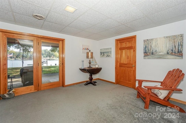 sitting room featuring a water view, a paneled ceiling, and carpet floors