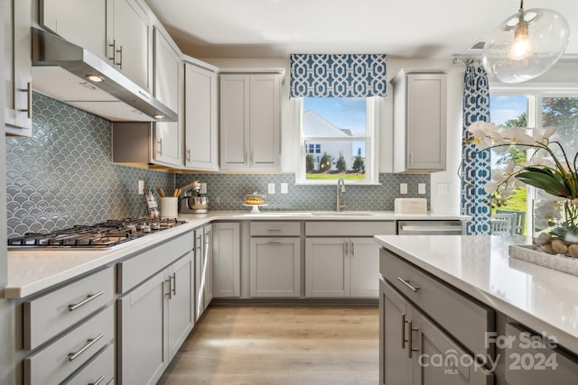 kitchen with appliances with stainless steel finishes, sink, decorative light fixtures, decorative backsplash, and light hardwood / wood-style flooring