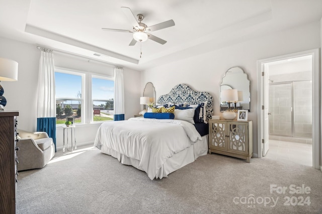 carpeted bedroom with ensuite bath, a tray ceiling, and ceiling fan