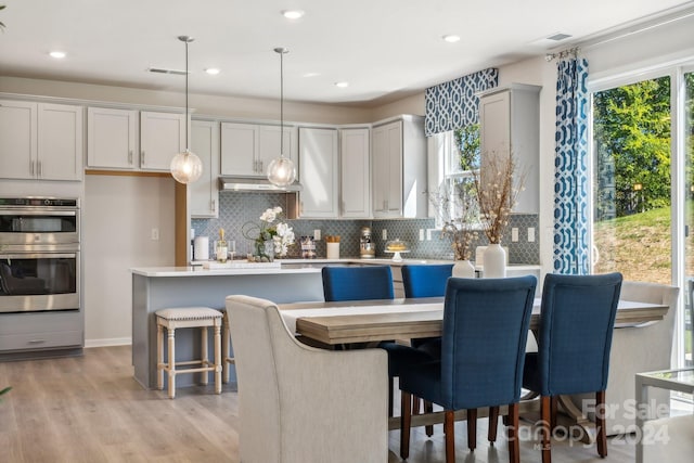 kitchen with stainless steel double oven, a kitchen island, backsplash, a breakfast bar, and pendant lighting