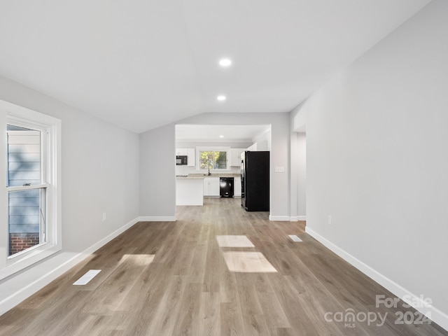 unfurnished living room with sink, light wood-type flooring, and vaulted ceiling