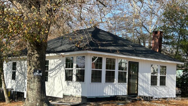view of property exterior featuring central AC, a chimney, and a shingled roof