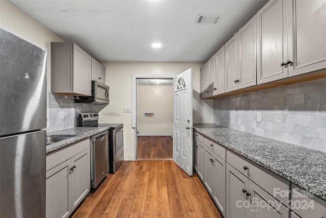 kitchen featuring decorative backsplash, stainless steel appliances, stone counters, and light hardwood / wood-style flooring