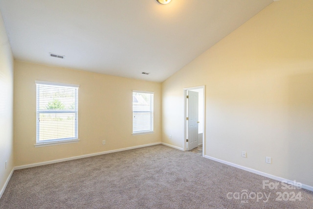 carpeted spare room with a wealth of natural light and vaulted ceiling