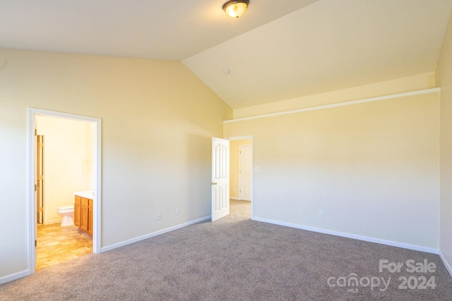 unfurnished bedroom with vaulted ceiling, light colored carpet, and ensuite bath