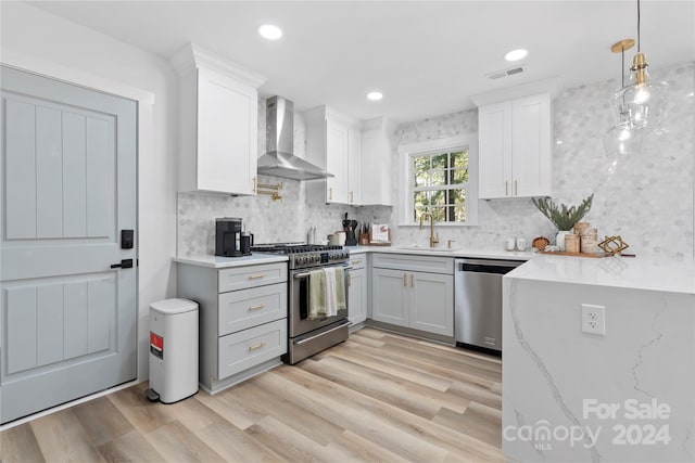 kitchen featuring appliances with stainless steel finishes, white cabinets, wall chimney range hood, and light wood-type flooring