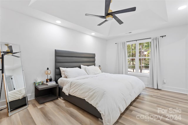 bedroom with a raised ceiling, light hardwood / wood-style floors, and ceiling fan