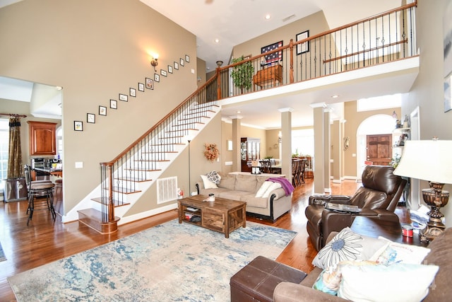 living room with decorative columns, a towering ceiling, plenty of natural light, and hardwood / wood-style floors