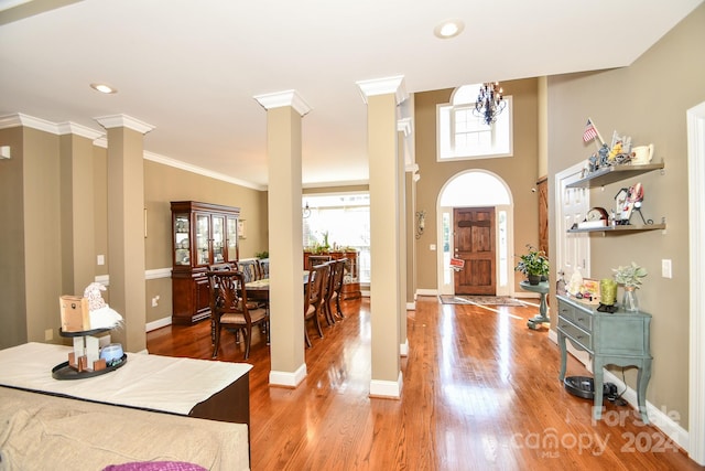 entryway with ornate columns, crown molding, wood-type flooring, and a chandelier