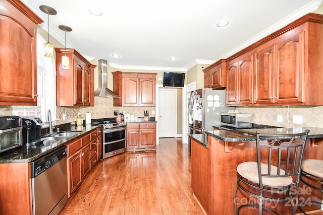 kitchen featuring hardwood / wood-style flooring, wall chimney exhaust hood, hanging light fixtures, sink, and appliances with stainless steel finishes