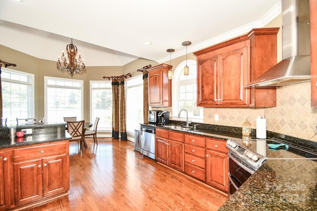 kitchen featuring wall chimney range hood, hanging light fixtures, stainless steel appliances, sink, and light wood-type flooring