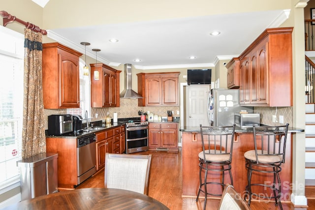 kitchen with sink, hanging light fixtures, stainless steel appliances, wall chimney exhaust hood, and dark hardwood / wood-style floors