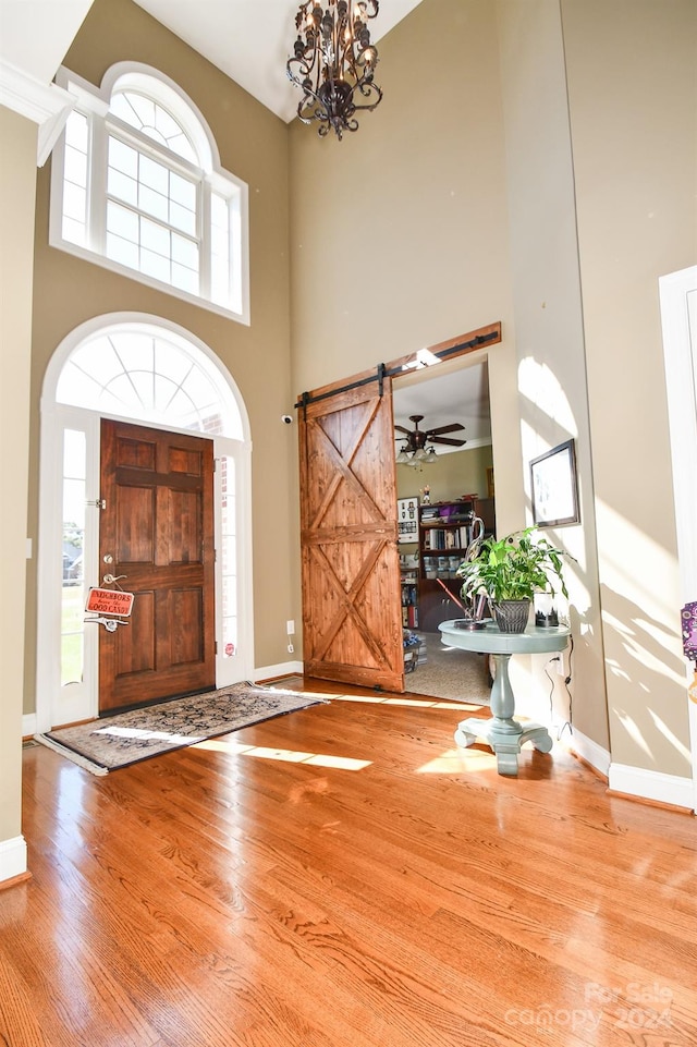 entrance foyer with hardwood / wood-style floors, a barn door, ceiling fan with notable chandelier, and a towering ceiling