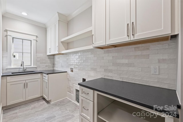 kitchen with decorative backsplash, white cabinetry, ornamental molding, and sink