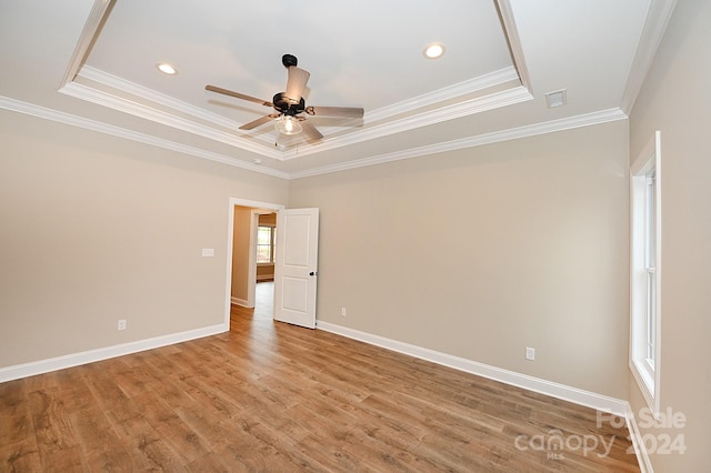 empty room with light wood-type flooring, a raised ceiling, ceiling fan, and crown molding