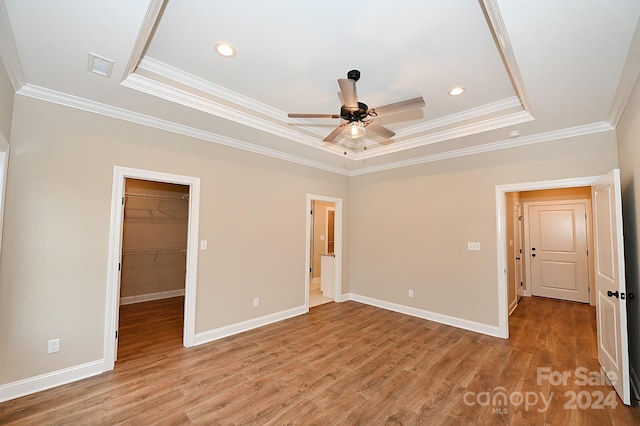 unfurnished bedroom featuring a tray ceiling, ceiling fan, a spacious closet, light hardwood / wood-style floors, and a closet