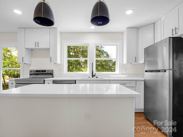 kitchen with sink, white cabinets, pendant lighting, appliances with stainless steel finishes, and light hardwood / wood-style floors