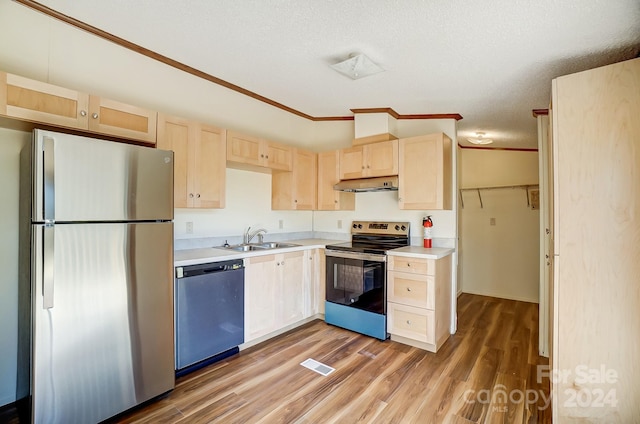 kitchen with appliances with stainless steel finishes, wood-type flooring, vaulted ceiling, ornamental molding, and sink