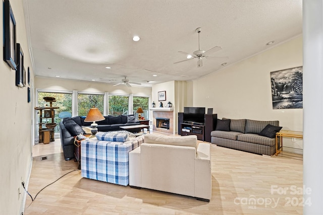 living room with ceiling fan, a tiled fireplace, a textured ceiling, and light hardwood / wood-style flooring