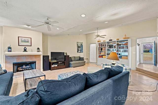 living room with light wood-type flooring, a fireplace, a textured ceiling, and ceiling fan