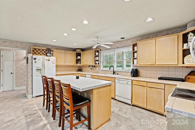 kitchen featuring tile counters, a center island, sink, light brown cabinets, and white appliances