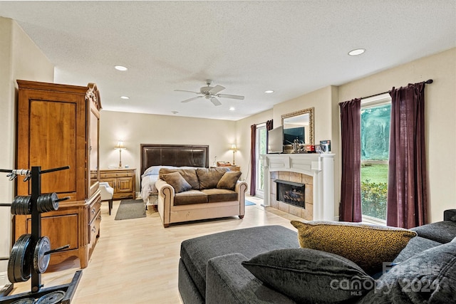 bedroom with a textured ceiling, light hardwood / wood-style floors, ceiling fan, and a tile fireplace