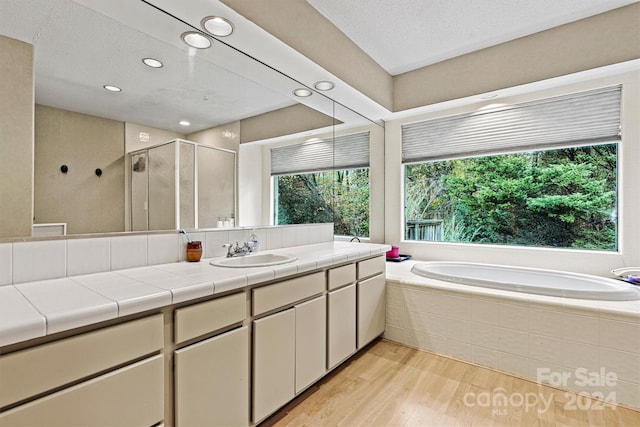 bathroom with independent shower and bath, wood-type flooring, vanity, and a textured ceiling