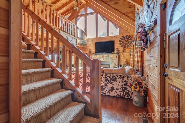 stairway featuring beamed ceiling, a stone fireplace, wood-type flooring, and wooden ceiling