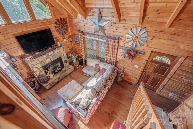 living room with wood ceiling, hardwood / wood-style flooring, wood walls, a stone fireplace, and lofted ceiling with beams