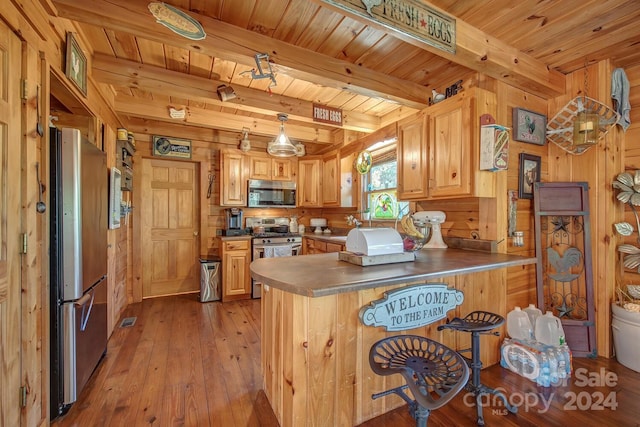 kitchen with appliances with stainless steel finishes, kitchen peninsula, wooden walls, and light wood-type flooring