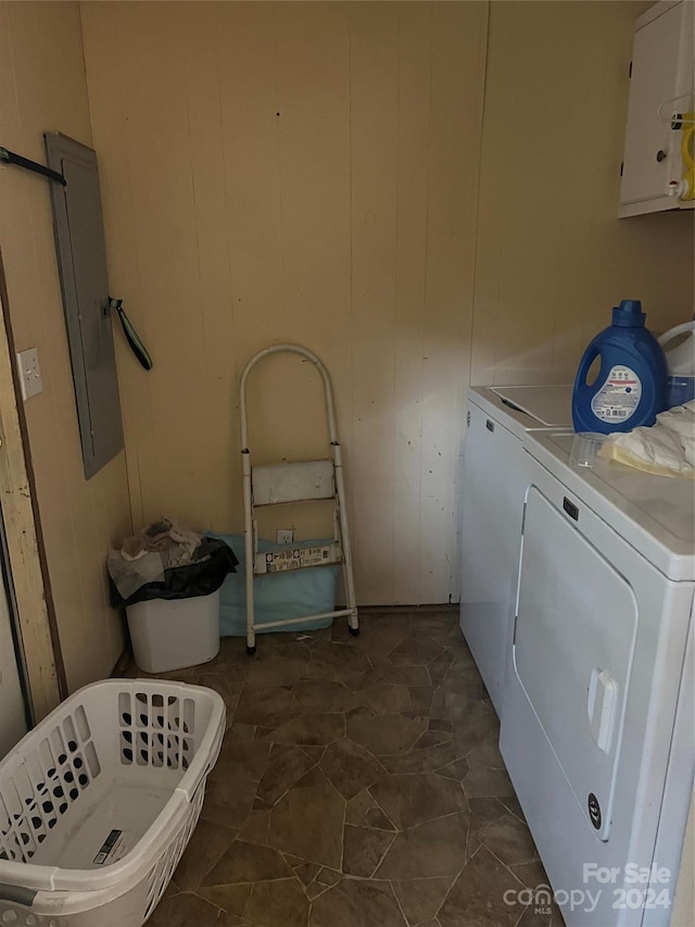 washroom with washer and dryer, electric panel, wooden walls, and dark tile patterned floors