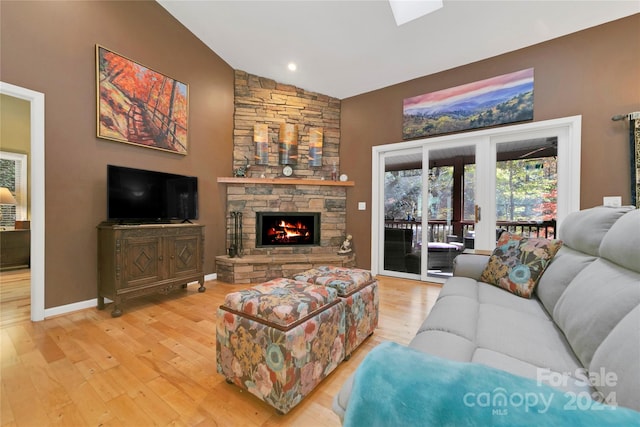 living room with vaulted ceiling, a stone fireplace, and wood-type flooring