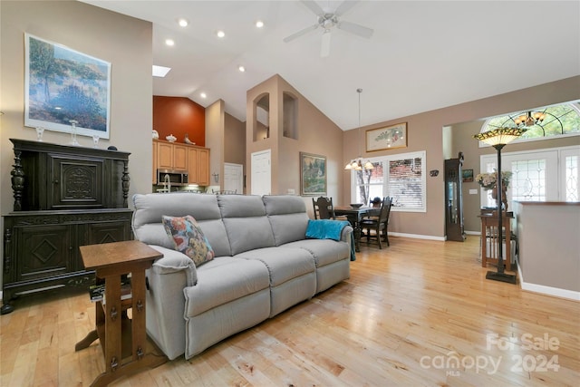 living room featuring high vaulted ceiling, ceiling fan with notable chandelier, and light wood-type flooring