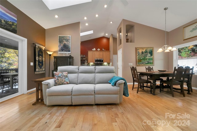 living room featuring light hardwood / wood-style floors, an inviting chandelier, high vaulted ceiling, and a skylight