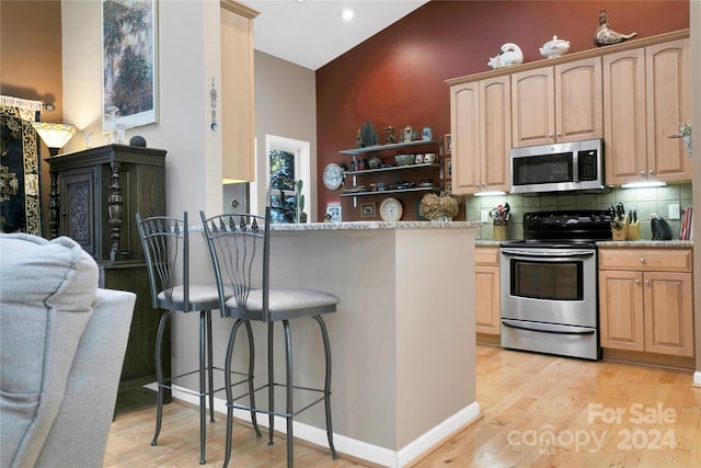 kitchen with light stone counters, light brown cabinetry, a kitchen bar, light hardwood / wood-style flooring, and stainless steel appliances