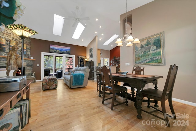 dining room featuring light hardwood / wood-style flooring, ceiling fan with notable chandelier, high vaulted ceiling, and a skylight