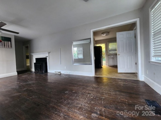 unfurnished living room featuring a fireplace with flush hearth, wood-type flooring, baseboards, a healthy amount of sunlight, and ceiling fan