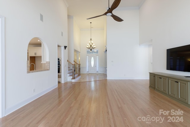 unfurnished living room with a towering ceiling, ornamental molding, light hardwood / wood-style flooring, and ceiling fan with notable chandelier