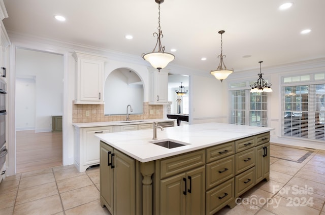 kitchen featuring an island with sink, ornamental molding, sink, decorative light fixtures, and tasteful backsplash