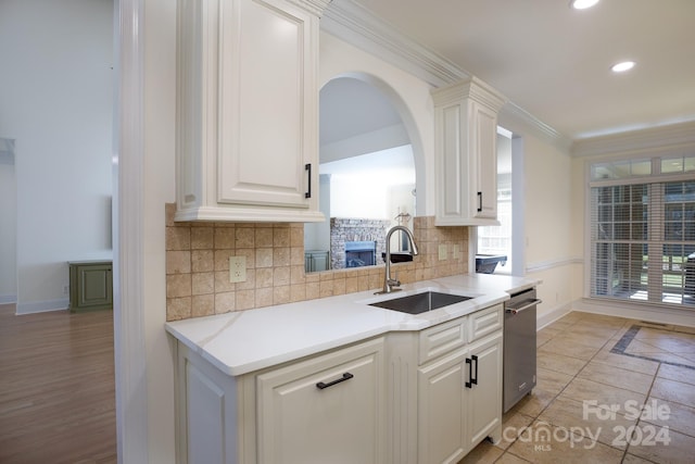 kitchen featuring decorative backsplash, dishwasher, crown molding, sink, and white cabinetry