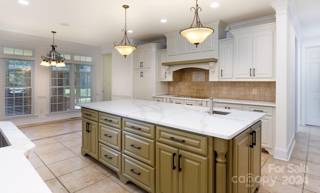 kitchen with decorative backsplash, a center island with sink, sink, crown molding, and decorative light fixtures