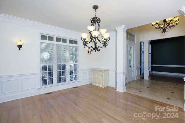 unfurnished dining area featuring an inviting chandelier, ornamental molding, ornate columns, and light wood-type flooring