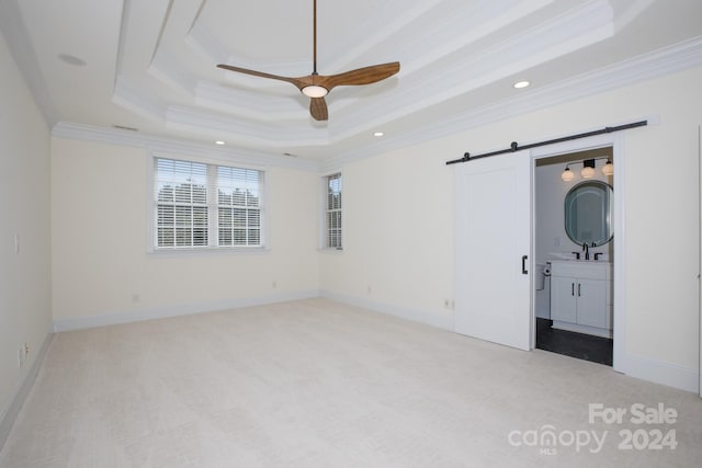 unfurnished bedroom with ceiling fan, a raised ceiling, ornamental molding, and a barn door