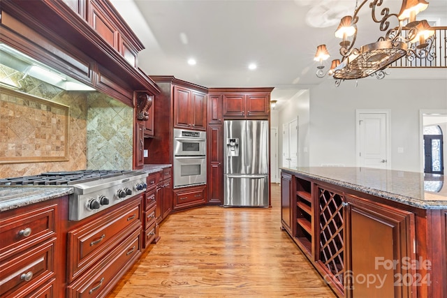 kitchen with backsplash, dark stone counters, light wood-type flooring, stainless steel appliances, and decorative light fixtures