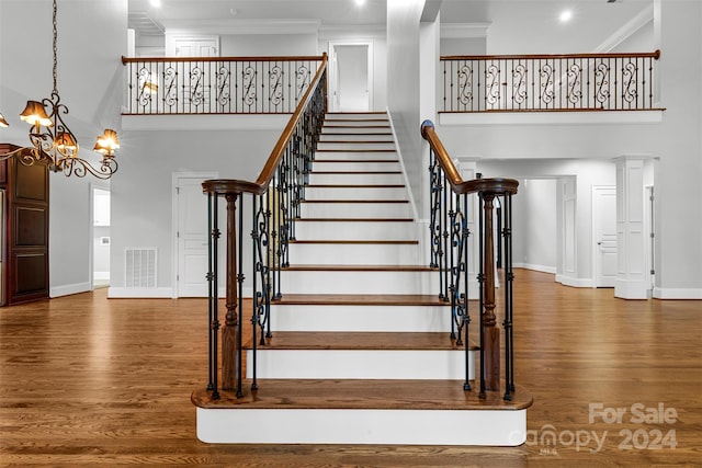 staircase featuring a towering ceiling, hardwood / wood-style floors, a chandelier, and ornamental molding