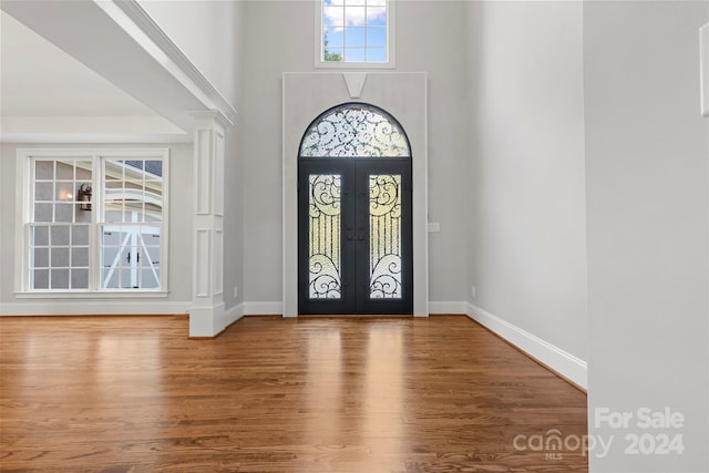 foyer featuring french doors, ornate columns, hardwood / wood-style flooring, and a towering ceiling