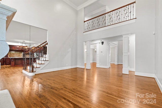 unfurnished living room with a towering ceiling, decorative columns, and light wood-type flooring